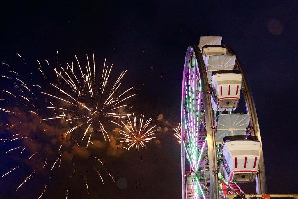 Ferris wheel overlooking fireworks in the night sky