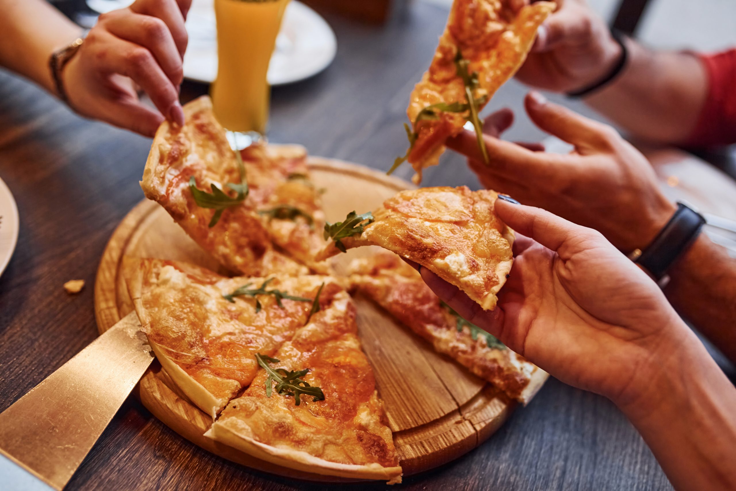 Close up view of people taking and eating pizza indoors together.
