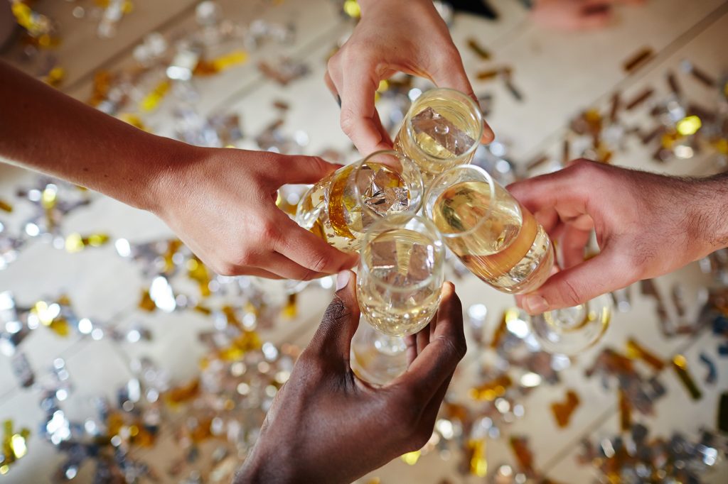 Hands toasting by flutes with sparkling champagne over floor covered with confetti