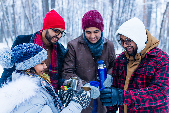 Happy young friends get warm with hot tea outside in the snow.