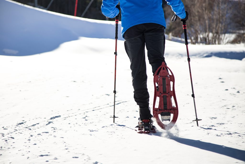Young man walking in snowshoes over winter background