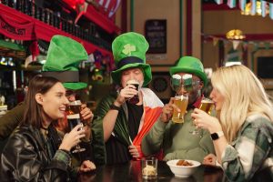 Group of friends in green hats sitting at the table drinking beer and celebrating Patricks Day in the bar
