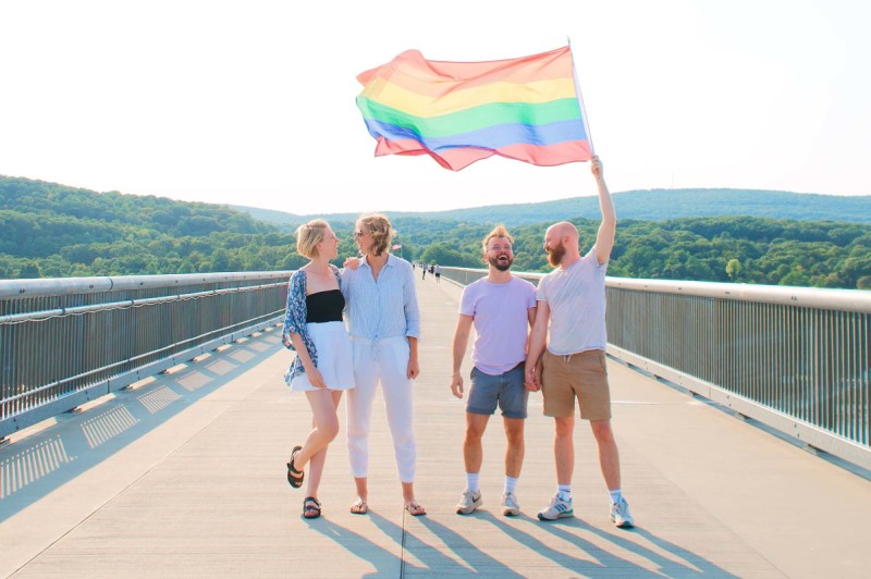 Four people waving a rainbow flag on the Walkway Over the Hudson in Poughkeepsie.