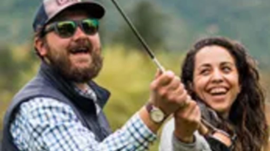A man and a woman smile as they practice casting a fly fishing rod.