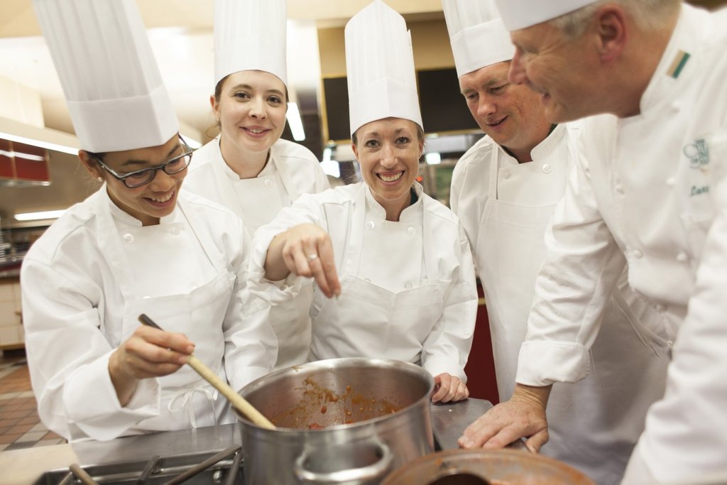 A group of chefs stands around a pot as one chef adds some spices in a kitchen at the Culinary Institute of America in Hyde Park.