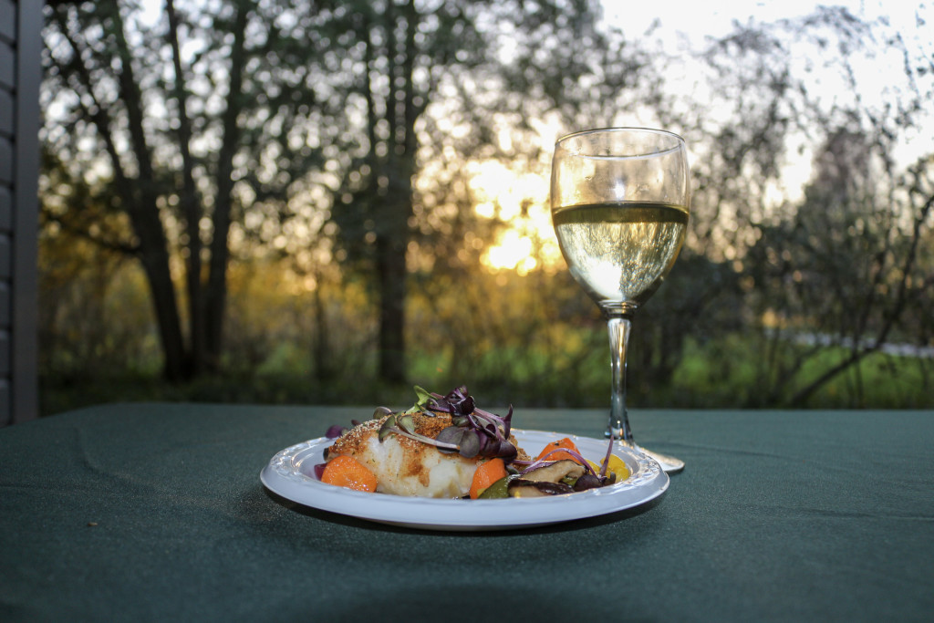 A delicious plate of food and a glass of white wine set on an outdoor table with the sun setting in the background at Locust Grove Estate in Poughkeepsie.