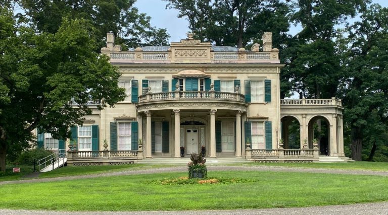 Montgomery Place, Bard College, Annandale-on-Hudson, a two story, beige mansion with green shutters with a manicured lawn and gravel driveway in front.