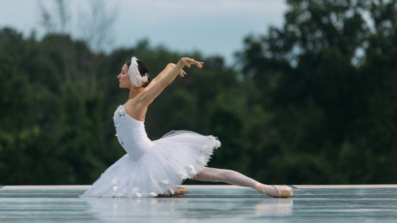 A caucasian female ballet dancer in a billowy white dress and a white headband performs on an outdoor stage on an overcast day at Kaatsbaan Cultural Park in Tivoli.