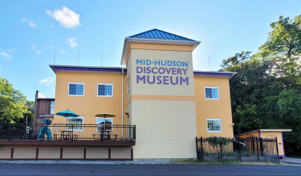 A photo of the exterior of the Mid-Hudson Discovery Museum, a two-story yellow building with purple and blue letters.