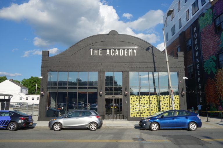 The gray and white, two-story exterior of The Academy in Poughkeepsie with cars parked in front.