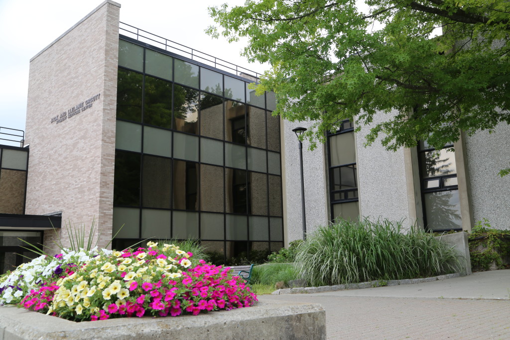 The exterior of one of the buildings at Dutchess Community College in Poughkeepsie, with trees and colorful flowers and bushes in front.