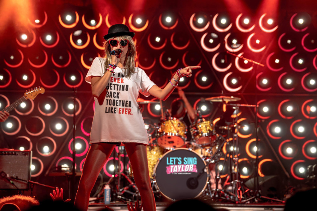 A photo of a musician dressed up to resemble Taylor Swift, with a black hat, white tee shirt, heart-shaped sunglasses and pink pants. The "Let's Sing Taylor: A Live Band Experience" is scheduled at the Bardavon 1869 Opera House in Poughkeepsie.