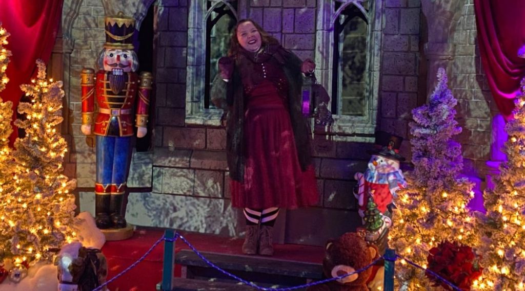 A woman in a red dress and brown boots smiles and carries a lantern as she walks past a life size wooden soldier at Kevin McCurdy's Holiday Spirit Festival at Bowdoin Park in Wappingers Falls. Photo courtesy of Imaginart Studios