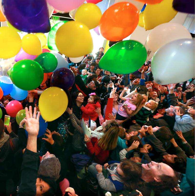 A crowd of parents with young children, some sitting on their parents' shoulders, cheer and celebrate as colorful balloons fall from the ceiling at the Mid Hudson Discovery Museum's New Year's at Noon event.