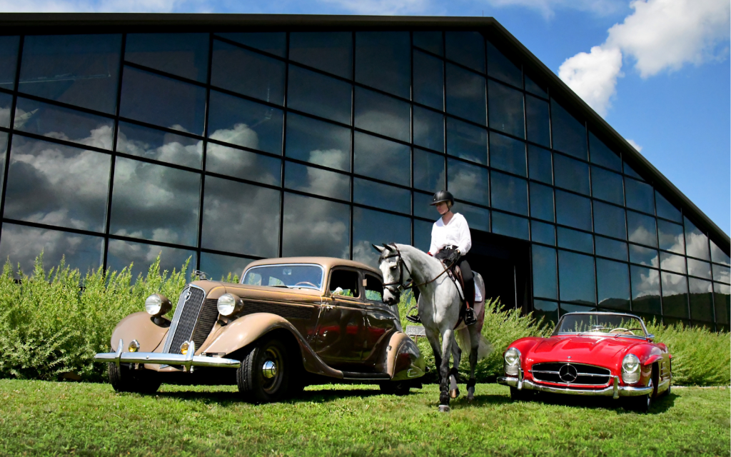 A horse and rider walk between two exotic automobiles.