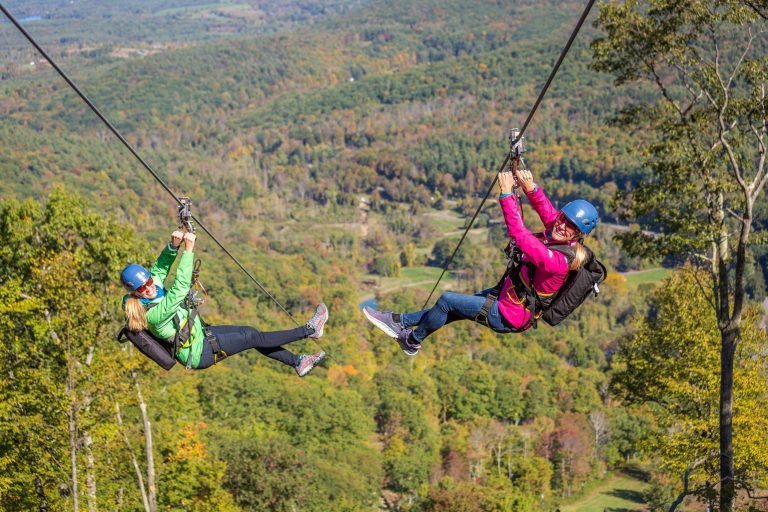 Two people zip lining with scenic views of the Berkshire Mountain range.