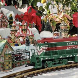A green and red model train runs along the track in front of a holiday village.