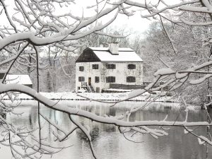 Philipsburg Manor covered in snow. In the foreground are snowy tree branches.