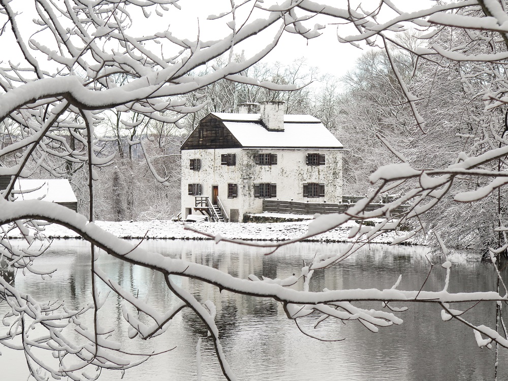 Philipsburg Manor covered in snow. In the foreground are snowy tree branches.