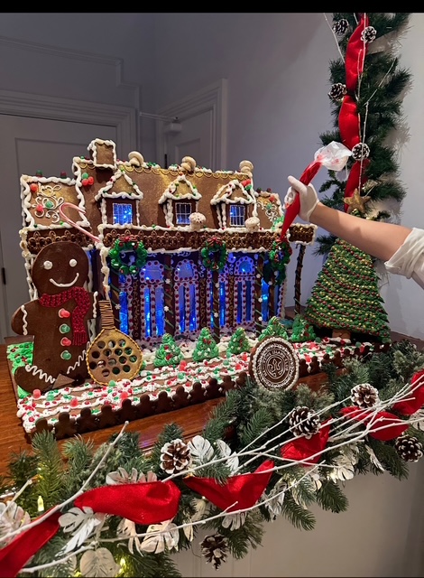 A baker decorates an elaborate gingerbread house.