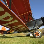 the side of a red-winged biplane preparing to take off of the grass path at Old Rhinebeck Aerodrome