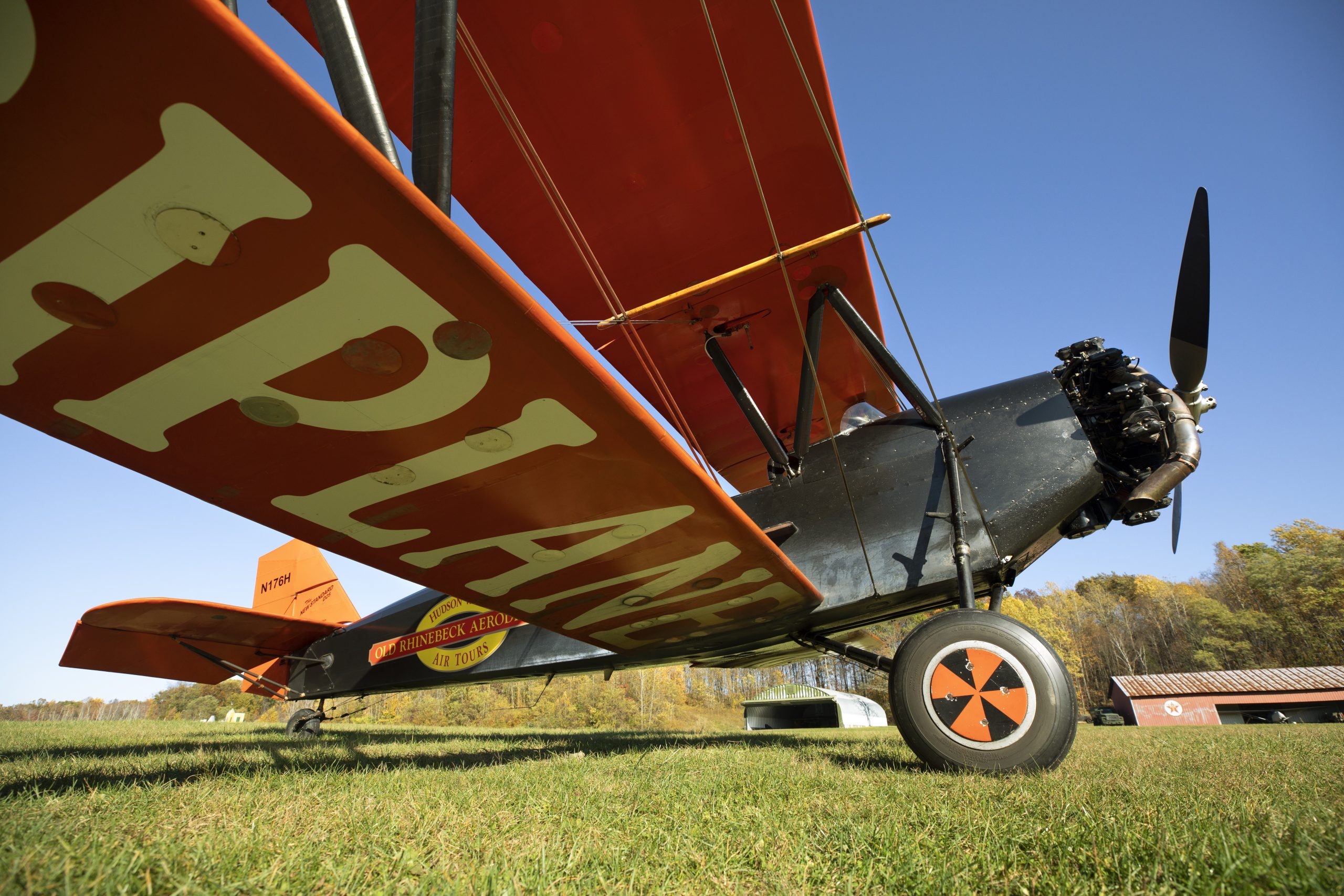 the side of a red-winged biplane preparing to take off of the grass path at Old Rhinebeck Aerodrome
