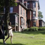 two women cross in front of a tall Victorian mansion the Wilderstein Estate which is a faded maroon color