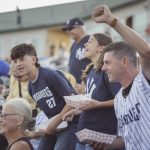 a crowd of people in pinstripe jerseys raise their fists and cheer for the Hudson Valley Renegades minor league baseball team at Heritage Financial Park