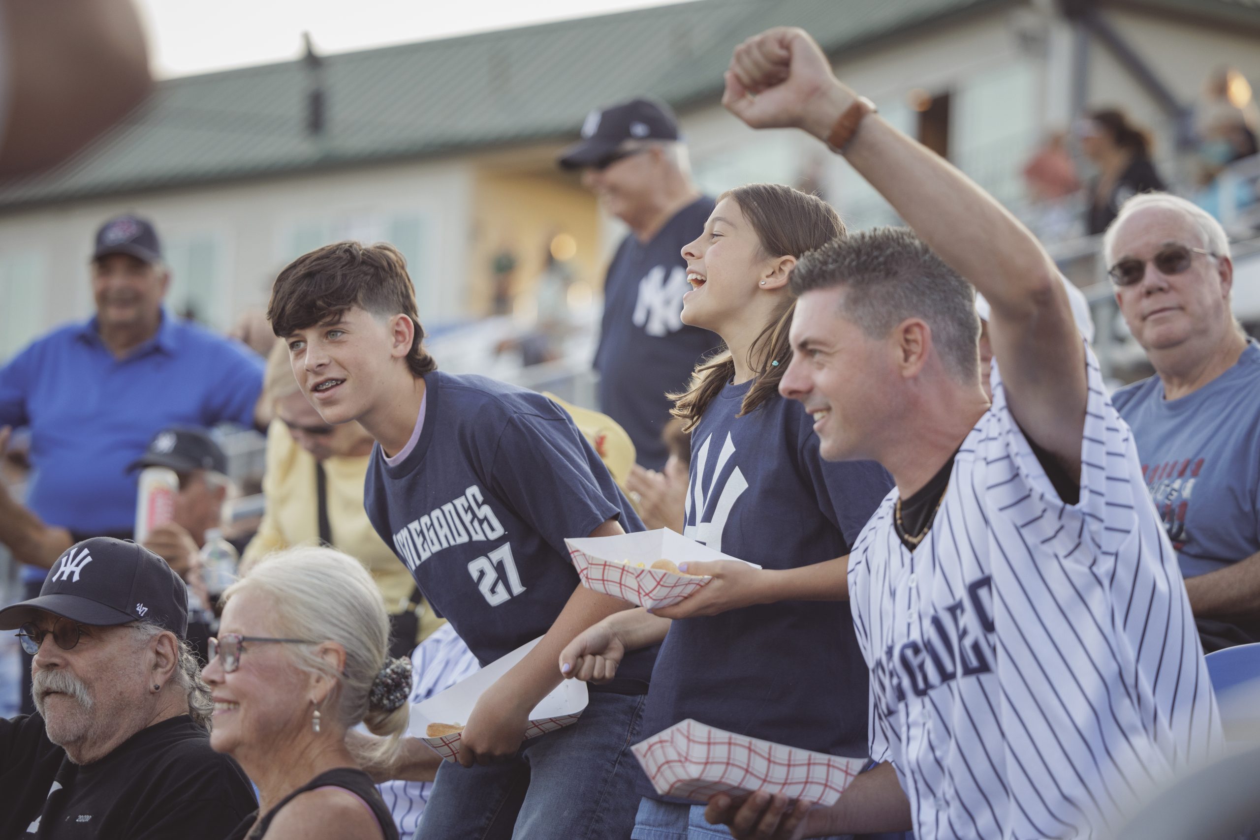 a crowd of people in pinstripe jerseys raise their fists and cheer for the Hudson Valley Renegades minor league baseball team at Heritage Financial Park