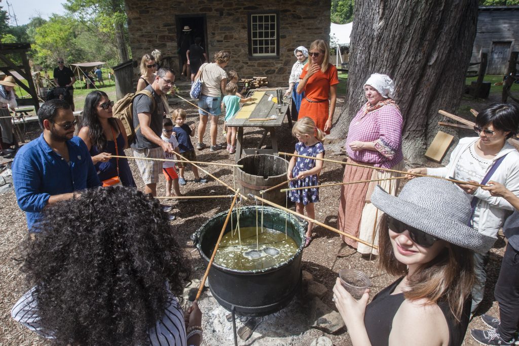 A group of people try candle dipping at Philipsburg Manor.