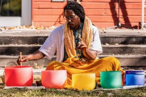A man sitting in the grass playing a rainbow-colored percussion instrument at the Beacon Flow Music and Wellness Festival. Photo by Alejandro Lopez.