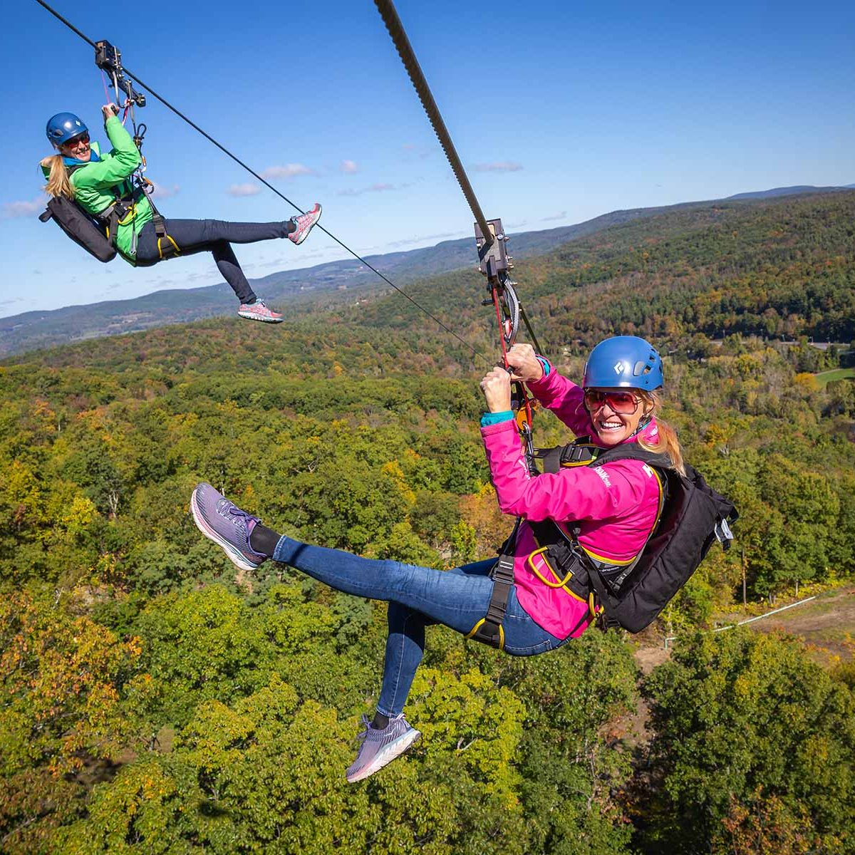 Two women ziplining over the mountains, Catamount Mountain Resort