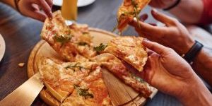 Close up view of people taking and eating pizza indoors together.