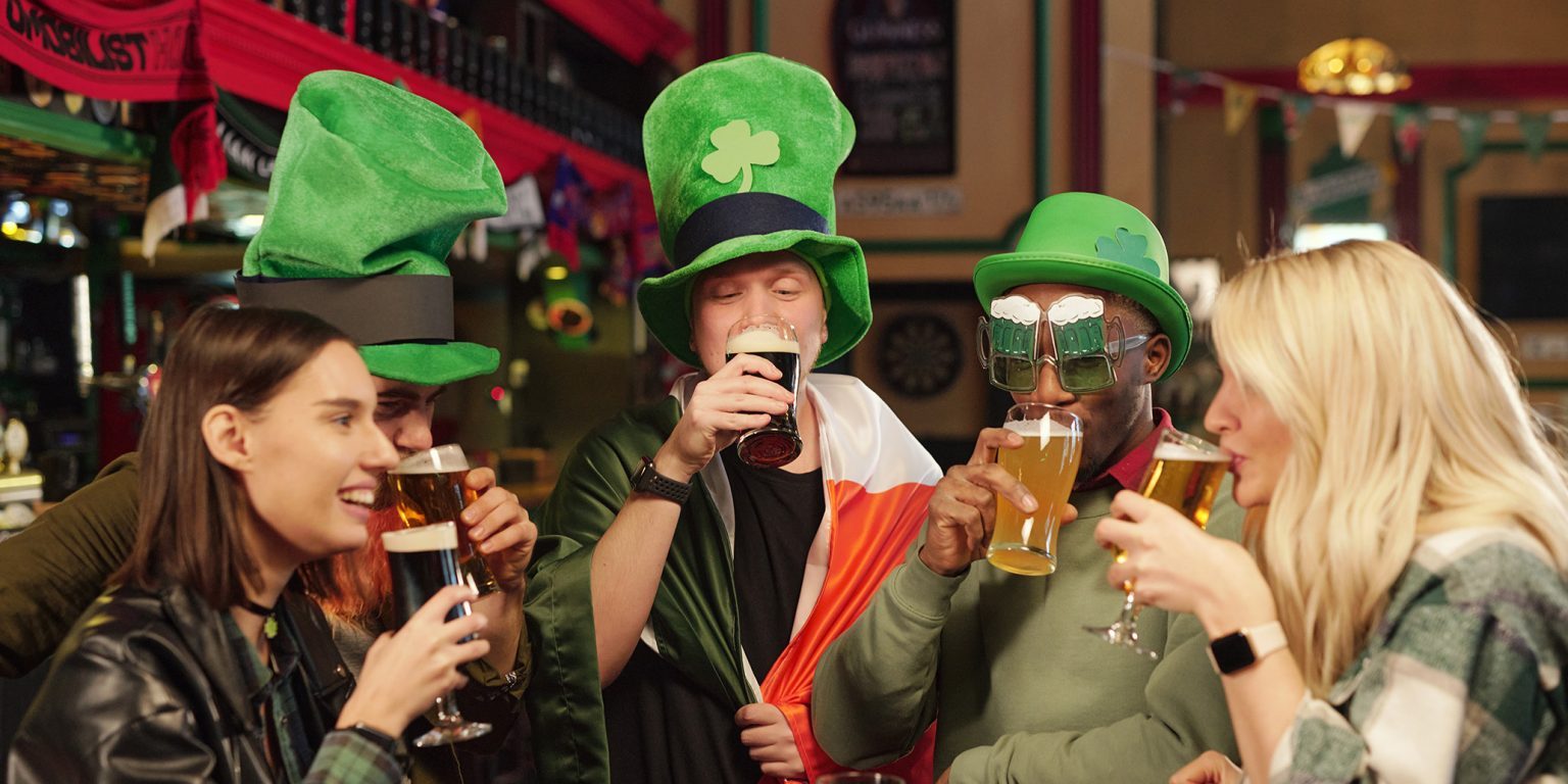 Group of friends in green hats sitting at the table drinking beer and celebrating Patricks Day in the bar