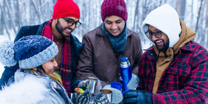 Happy young friends get warm with hot tea outside in the snow.