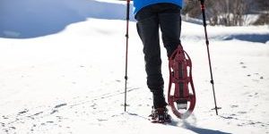 Young man walking in snowshoes over winter background